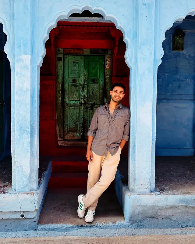 Aman leaning in a red doorway framed by a blue arched wall